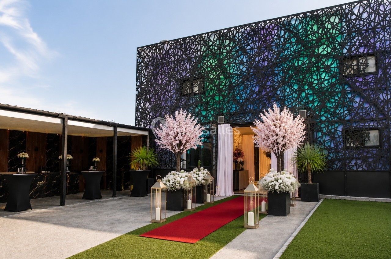 Façade décorée d'un bâtiment avec tapis rouge, lanternes, arbres fleuris et aménagement extérieur soigné.