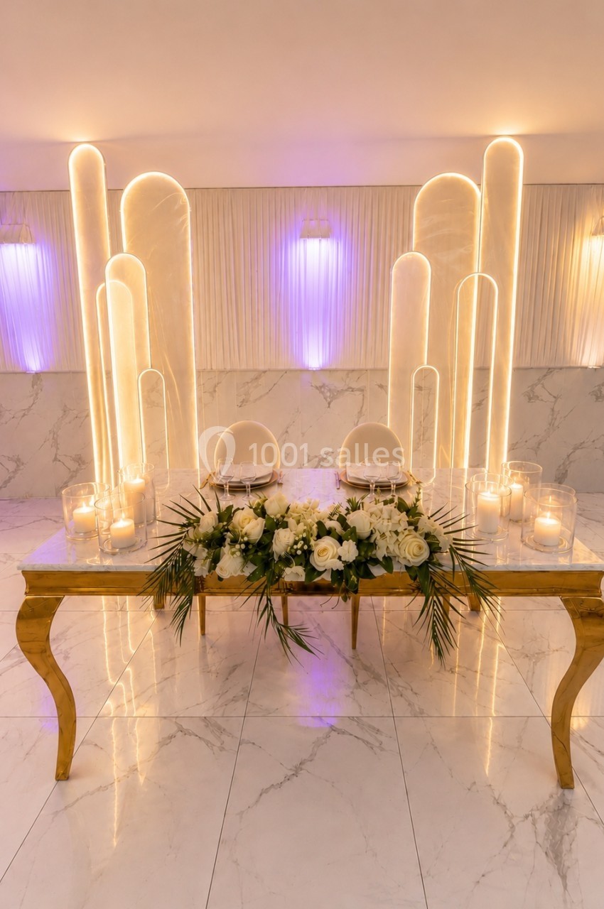 Table décorative avec fleurs blanches, bougies et arches lumineuses en arrière-plan dans un espace élégant.