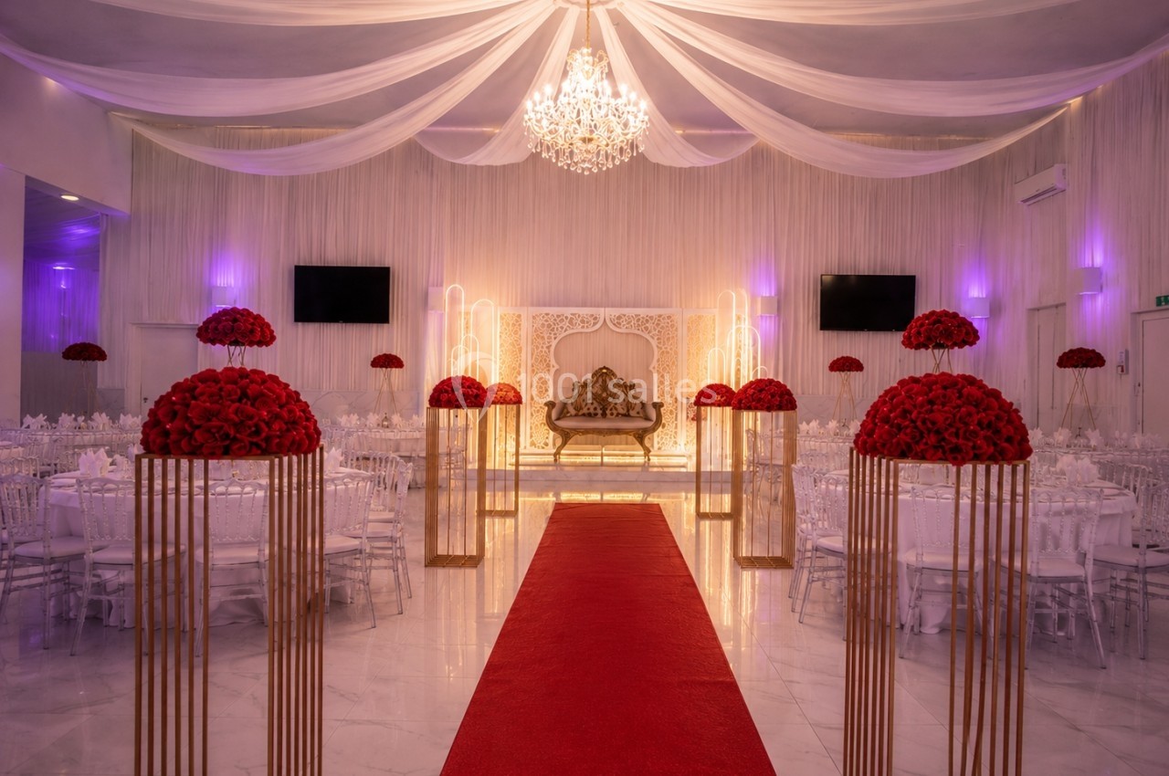 Salle de réception décorée avec un tapis rouge, des bouquets de roses rouges et un canapé doré sous un lustre.
