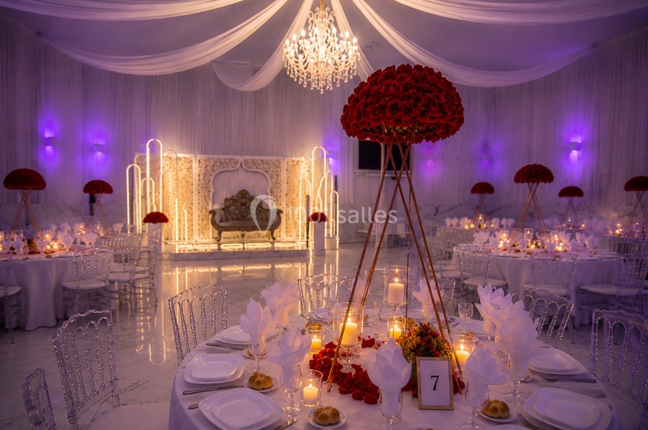 Salle de réception décorée avec des tables élégantes, des chandelles, des roses rouges et un éclairage violet tamisé.