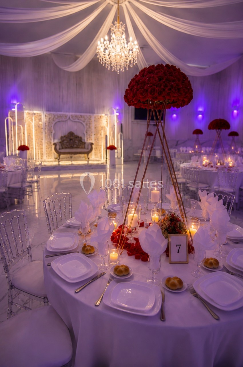 Salle de réception élégante avec tables décorées, centre de table floral rouge et éclairage tamisé.