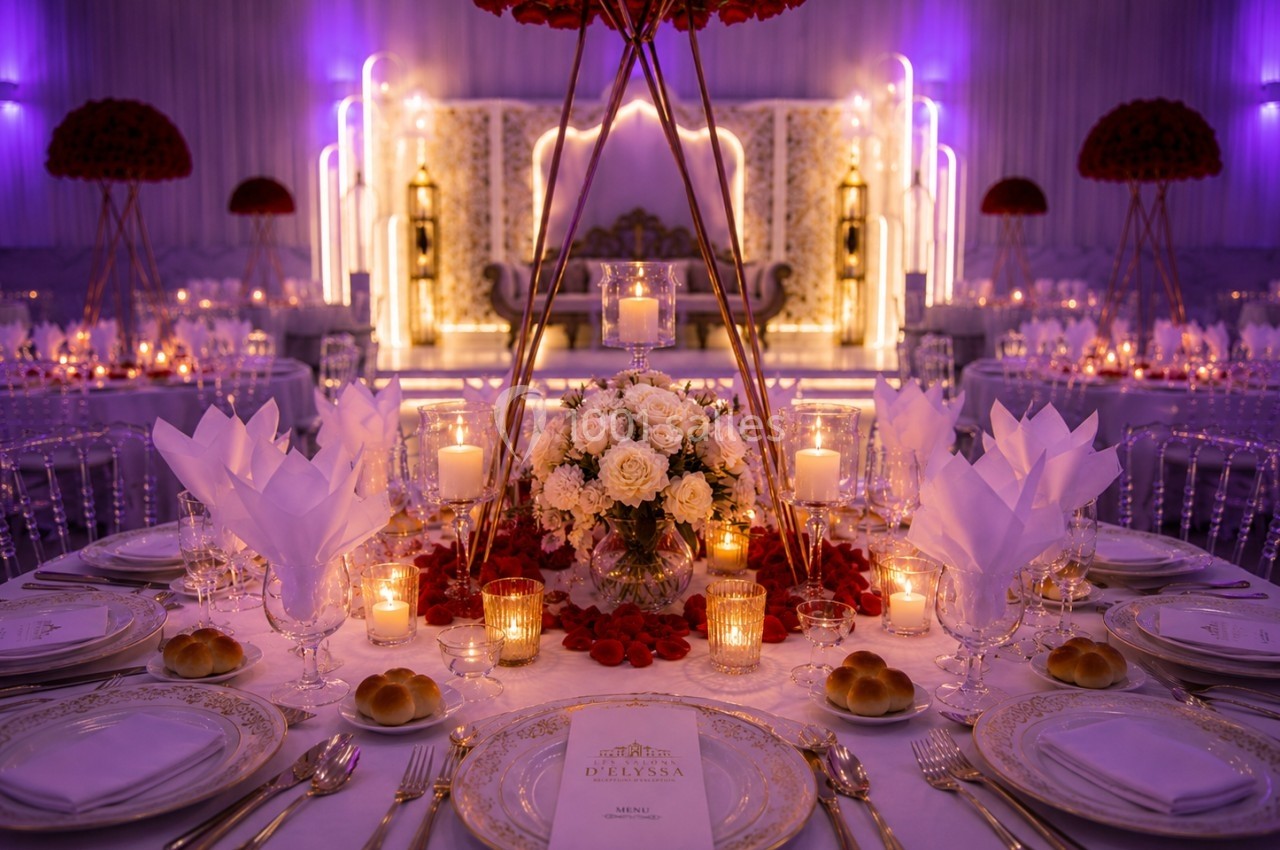 Table de réception élégamment dressée avec des fleurs, bougies allumées et vaisselle raffinée dans une salle illuminée.