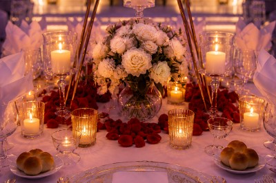 Table de réception élégamment décorée avec des fleurs blanches et rouges, bougies allumées et vaisselle raffinée.