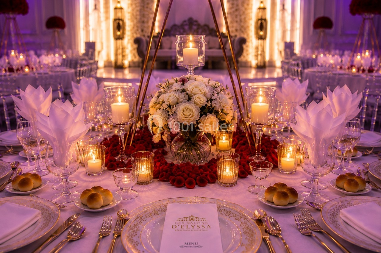 Table de réception élégamment décorée avec des fleurs blanches et rouges, bougies allumées et vaisselle raffinée.