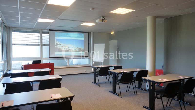 Salle de formation lumineuse avec tables, chaises, vidéoprojecteur et tableau blanc.