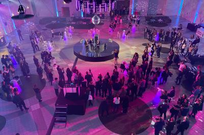Salle circulaire avec tables rondes dressées, nappes grises et serviettes vertes, entourée de baies vitrées donnant sur des…