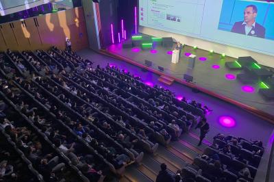 Salle circulaire avec tables rondes dressées, nappes grises et serviettes vertes, entourée de baies vitrées donnant sur des…