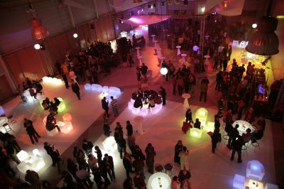 Salle circulaire avec tables rondes dressées, nappes grises et serviettes vertes, entourée de baies vitrées donnant sur des…