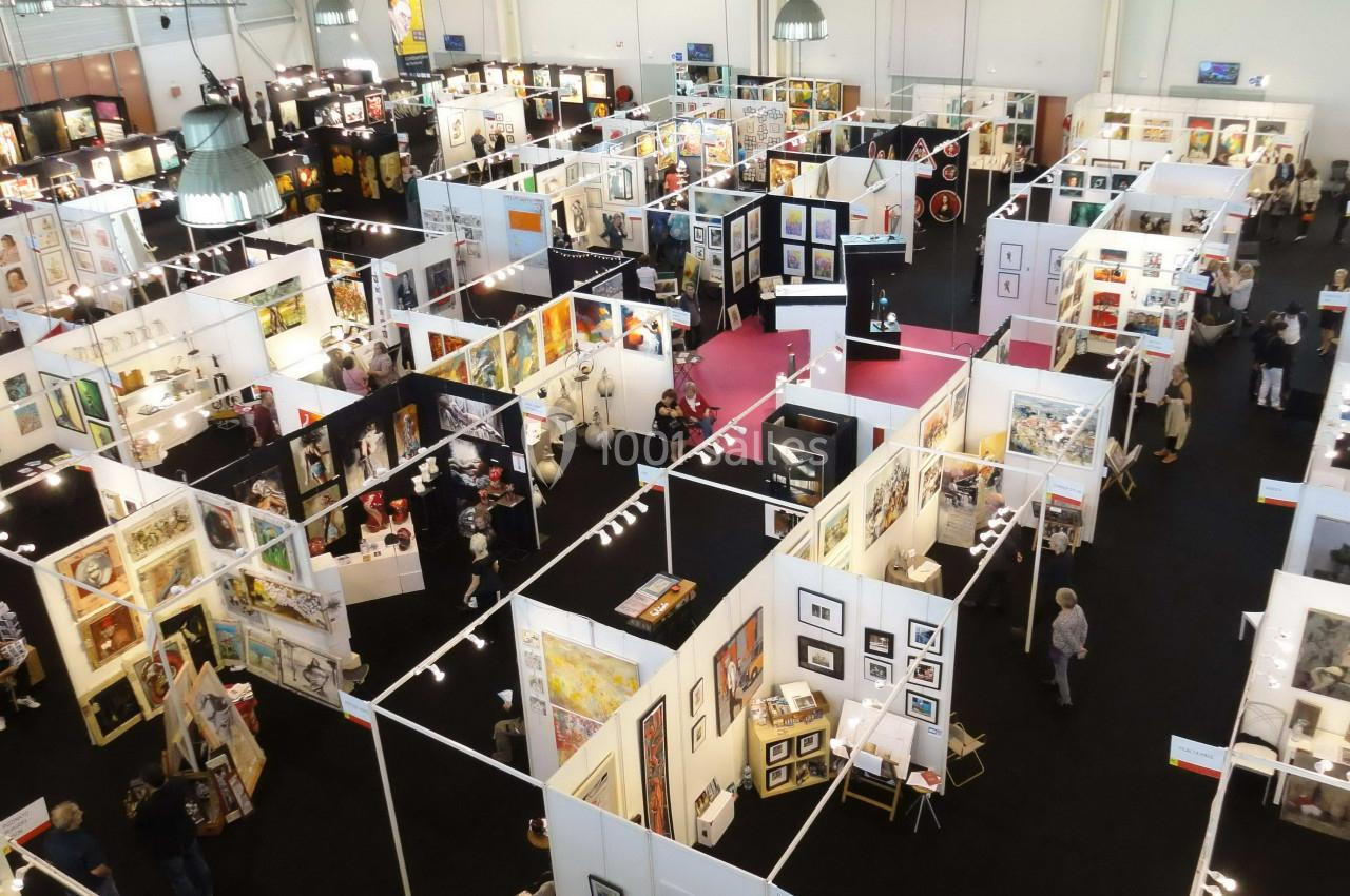 Vue aérienne d'une exposition artistique avec des stands présentant des œuvres variées et des visiteurs circulant.