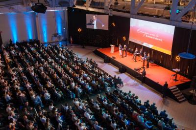Salle circulaire avec tables rondes dressées, nappes grises et serviettes vertes, entourée de baies vitrées donnant sur des…