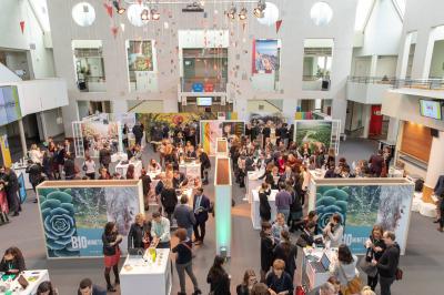 Salle circulaire avec tables rondes dressées, nappes grises et serviettes vertes, entourée de baies vitrées donnant sur des…