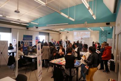 Salle circulaire avec tables rondes dressées, nappes grises et serviettes vertes, entourée de baies vitrées donnant sur des…