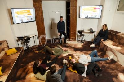 Personnes rassemblées sous une tente verte sur une terrasse, avec des plantes en pot et des clochers en arrière-plan.
