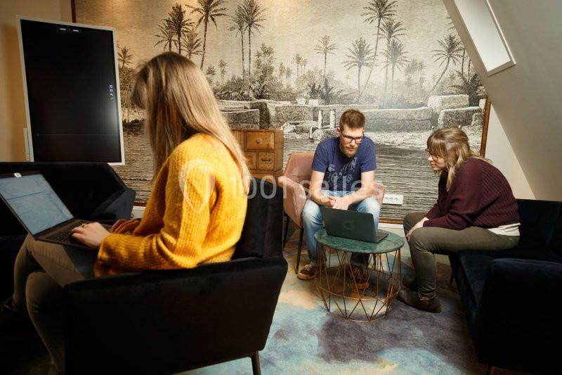 Trois personnes travaillent sur des ordinateurs portables dans un salon avec une décoration murale représentant un paysage…