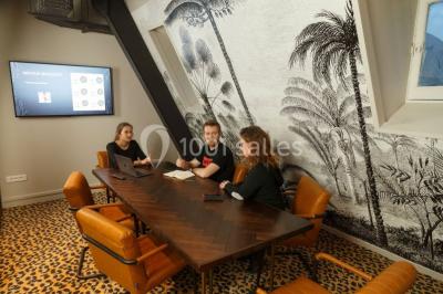 Personnes rassemblées sous une tente verte sur une terrasse, avec des plantes en pot et des clochers en arrière-plan.