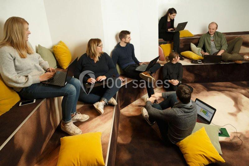 Un groupe de personnes assises sur des gradins, travaillant sur des ordinateurs portables dans un espace informel.