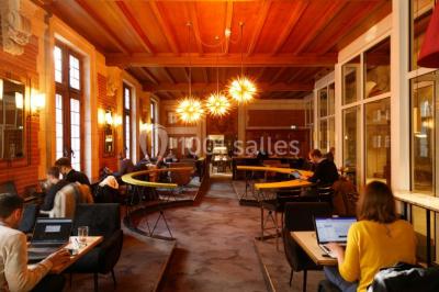 Personnes rassemblées sous une tente verte sur une terrasse, avec des plantes en pot et des clochers en arrière-plan.