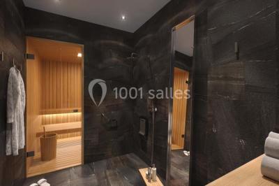 Salle de bain moderne avec murs sombres, douche à l'italienne et vue sur un sauna en bois éclairé.