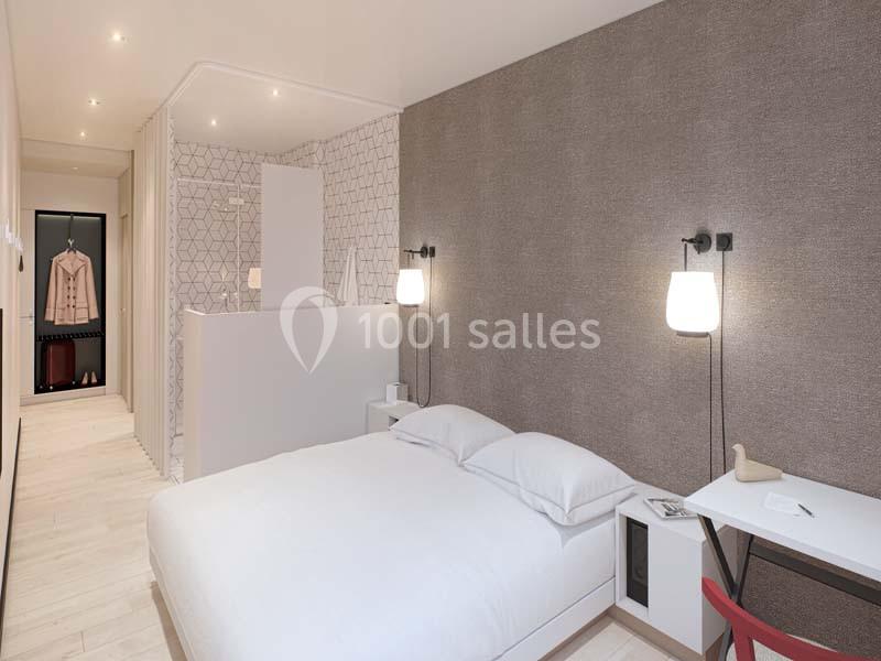 Chambre moderne avec lit double, bureau, éclairage doux et penderie ouverte visible en arrière-plan.