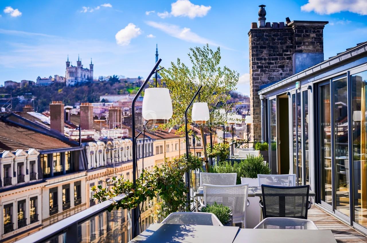 Terrasse aménagée avec vue sur les toits de la ville et la basilique de Fourvière sous un ciel bleu.
