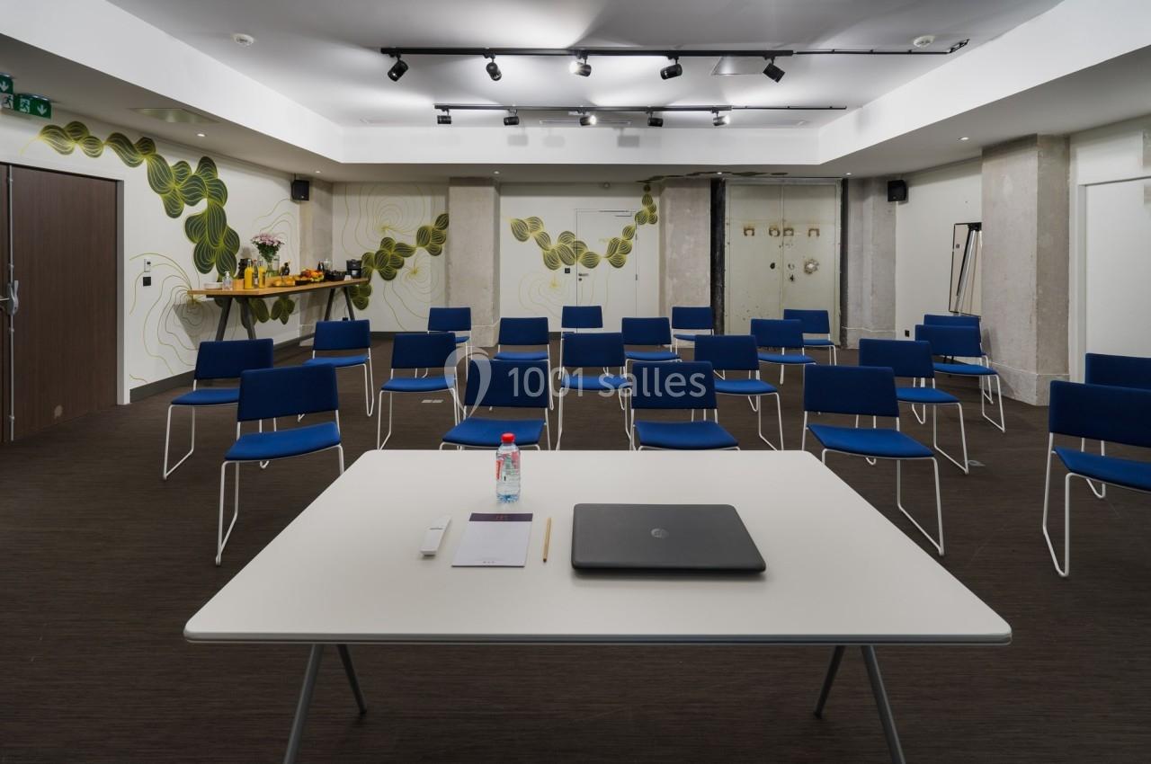 Salle de réunion avec des chaises alignées, une table à l'avant contenant un ordinateur portable et des fournitures.