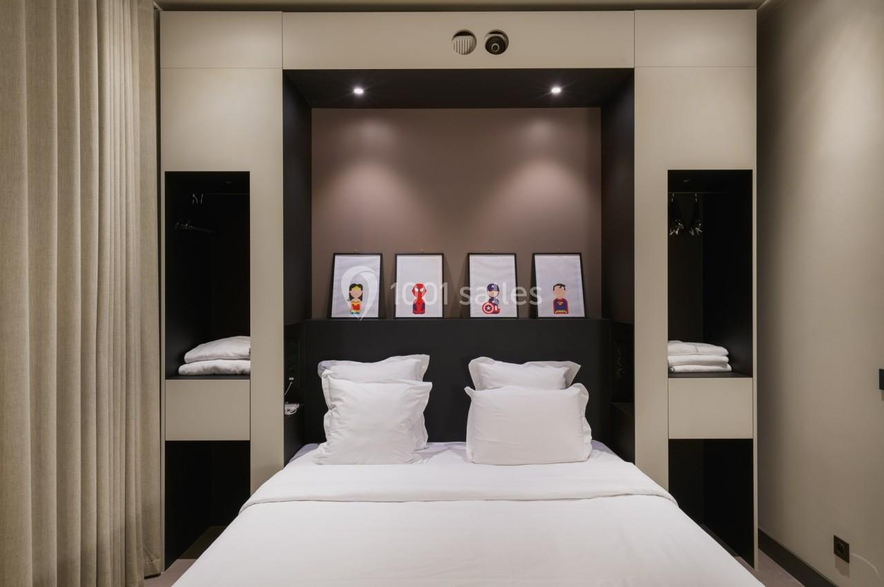 Lit double avec oreillers blancs, encadré par des étagères intégrées, et quatre illustrations encadrées au mur.