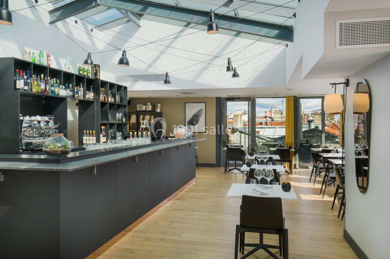 Intérieur lumineux d'un restaurant avec un bar moderne, des tables dressées et une vue sur les toits par de grandes baies…