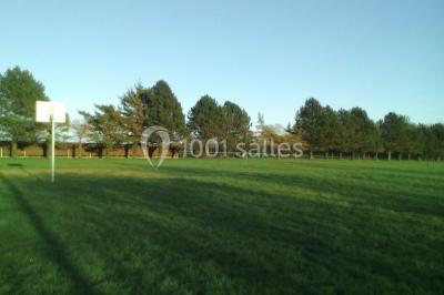Salle lumineuse avec deux rangées de tables et chaises bleues, grandes fenêtres et portes vitrées sur les côtés.