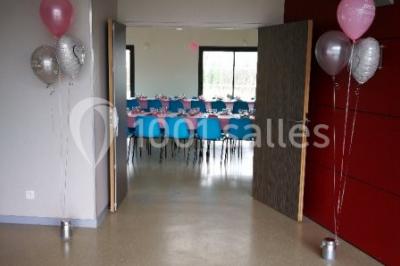 Salle lumineuse avec deux rangées de tables et chaises bleues, grandes fenêtres et portes vitrées sur les côtés.
