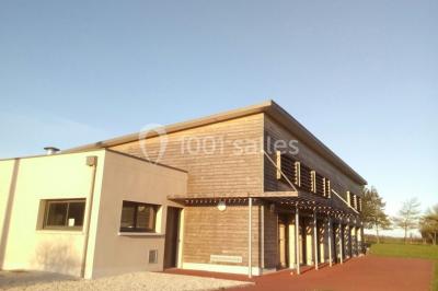 Salle lumineuse avec deux rangées de tables et chaises bleues, grandes fenêtres et portes vitrées sur les côtés.