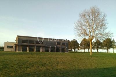Salle lumineuse avec deux rangées de tables et chaises bleues, grandes fenêtres et portes vitrées sur les côtés.