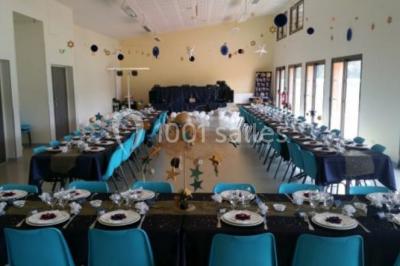 Salle lumineuse avec deux rangées de tables et chaises bleues, grandes fenêtres et portes vitrées sur les côtés.