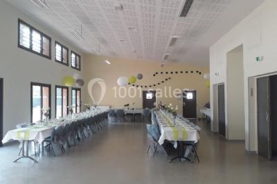 Salle lumineuse avec deux rangées de tables et chaises bleues, grandes fenêtres et portes vitrées sur les côtés.