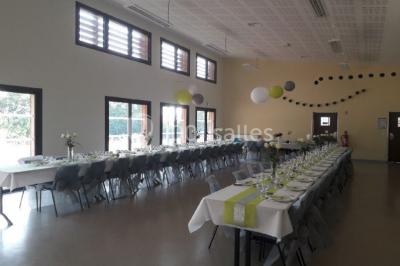 Salle lumineuse avec deux rangées de tables et chaises bleues, grandes fenêtres et portes vitrées sur les côtés.