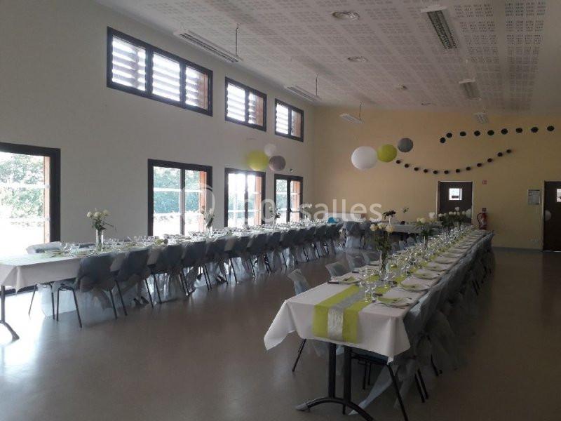 Salle de réception lumineuse avec de longues tables dressées pour un événement, décorées de nappes blanches et de touches…