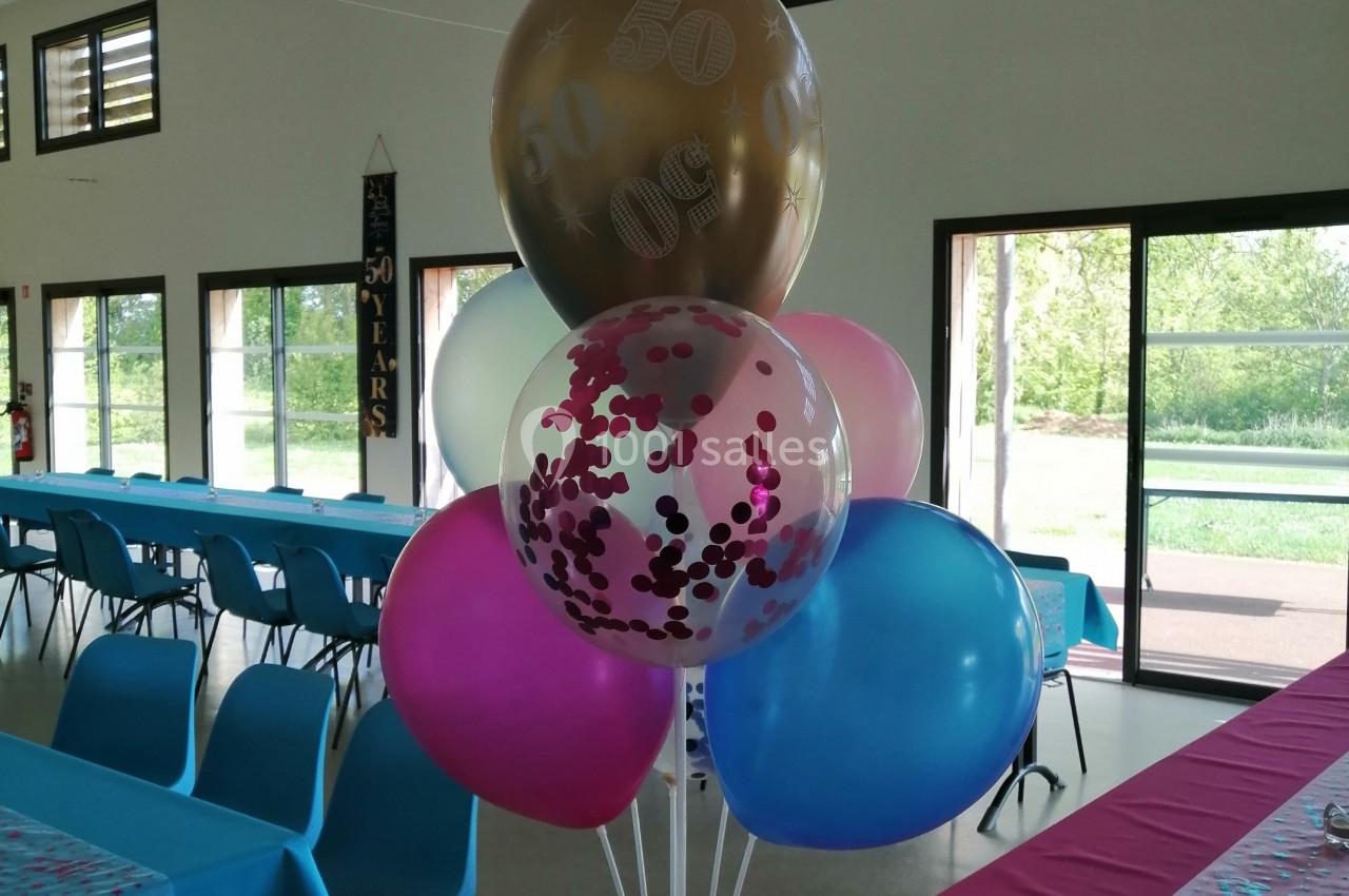 Bouquet de ballons colorés décorant une salle avec des tables dressées et une vue sur l'extérieur.