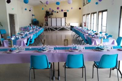 Salle lumineuse avec deux rangées de tables et chaises bleues, grandes fenêtres et portes vitrées sur les côtés.