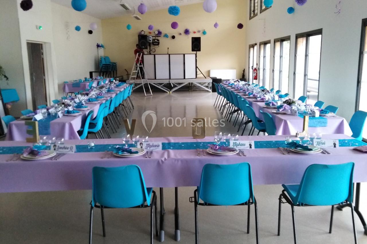 Salle décorée pour un événement avec tables dressées en violet et bleu, chaises alignées et espace pour une piste de danse.