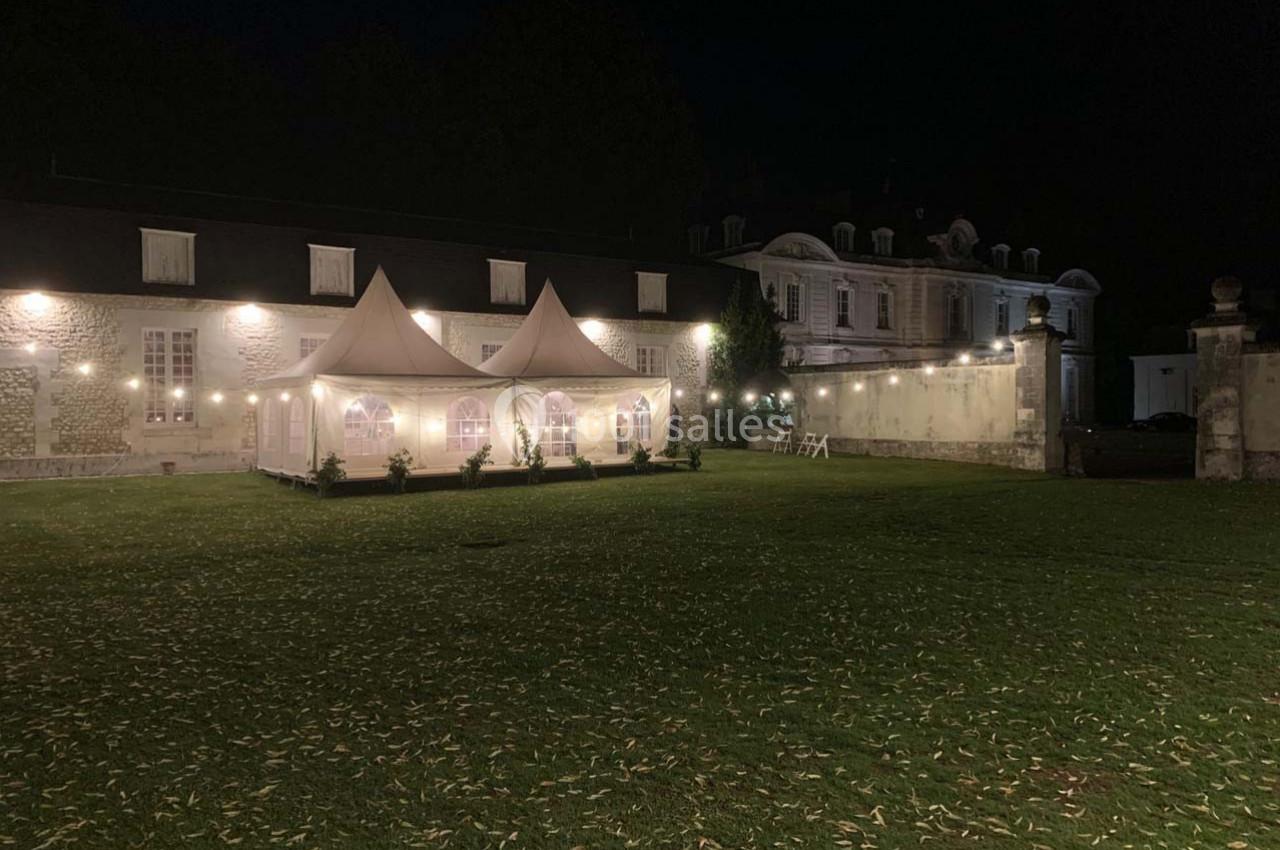 Tente éclairée installée sur une pelouse devant un bâtiment ancien, dans un cadre nocturne.