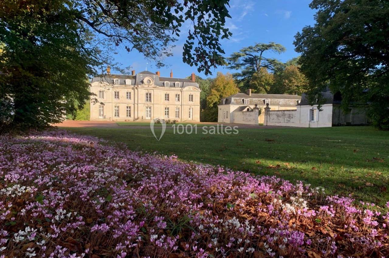 Façade d'un château entouré de pelouses, avec des fleurs roses au premier plan et des arbres en arrière-plan.