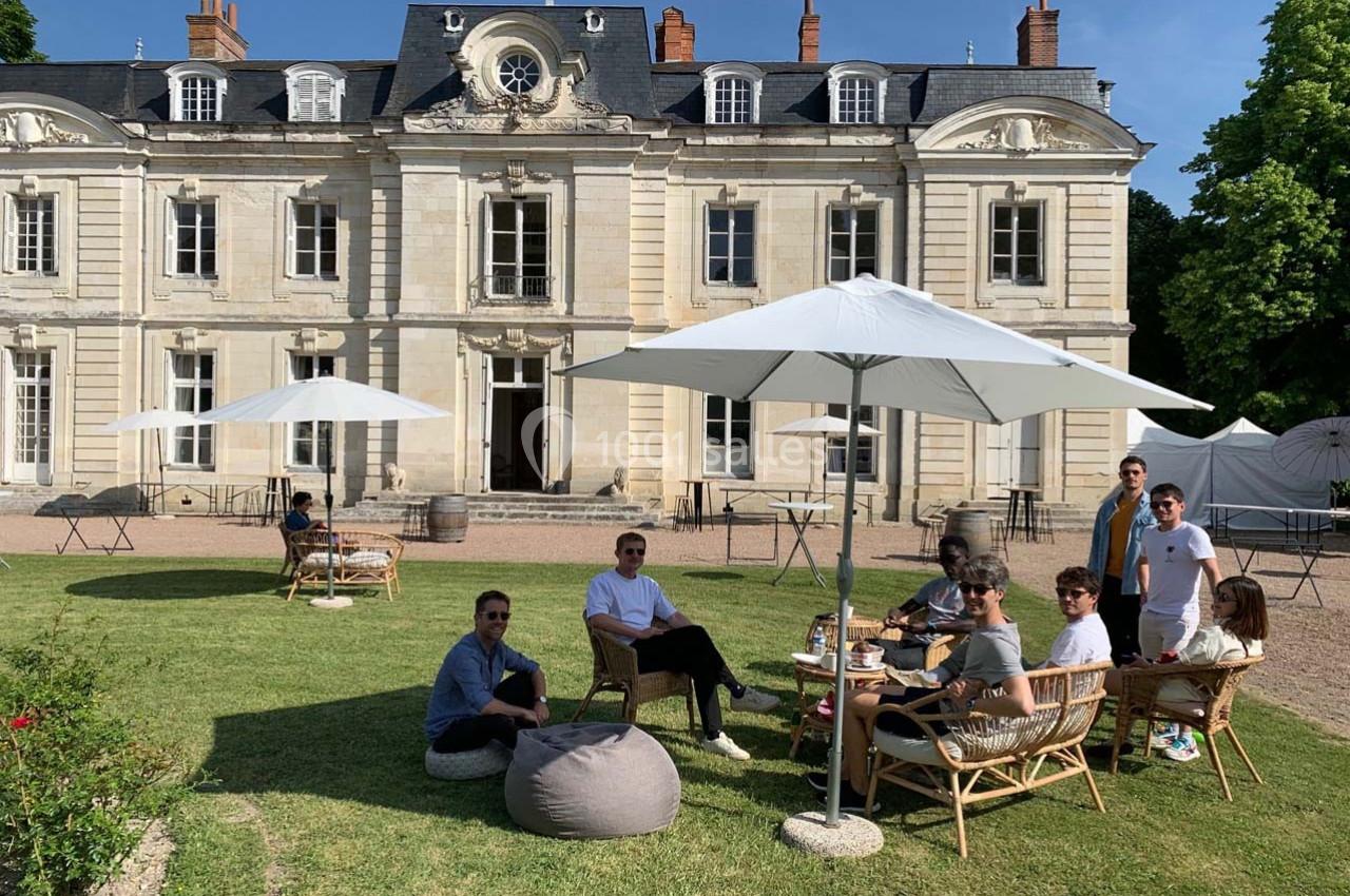 Groupe de personnes assises sous des parasols dans le jardin d'un château, par une journée ensoleillée.