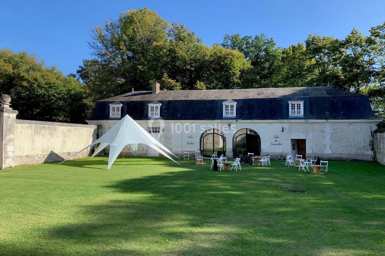 Pelouse verdoyante avec une grande tente blanche devant un bâtiment en pierre entouré d'arbres.