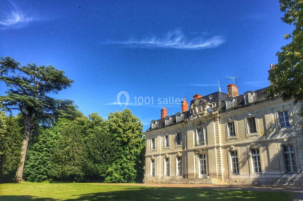 Façade d'un bâtiment ancien en pierre entouré d'arbres et d'une pelouse, sous un ciel bleu dégagé.