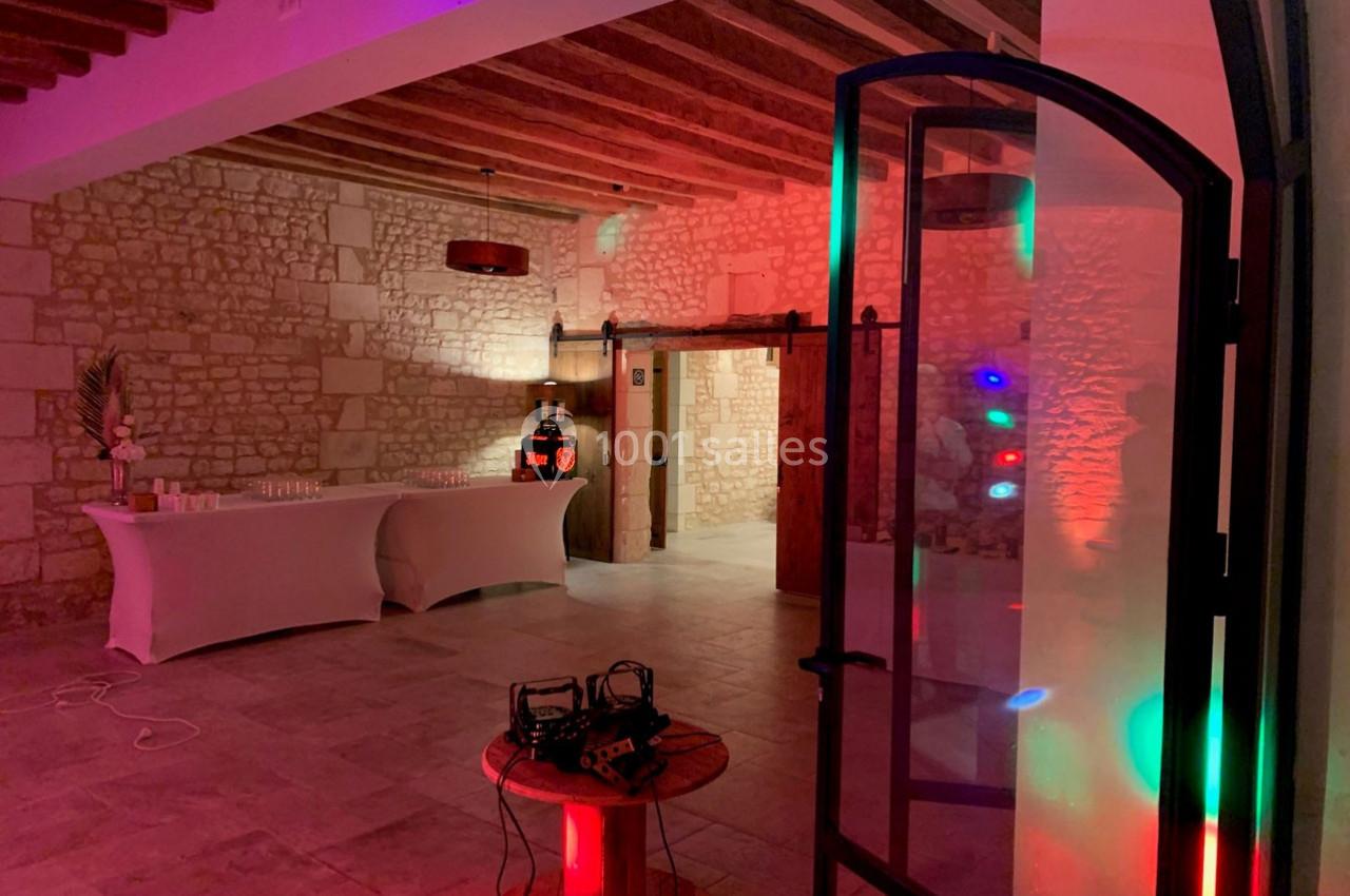 Salle en pierre éclairée par des lumières colorées, avec une table dressée et des équipements audio visibles.