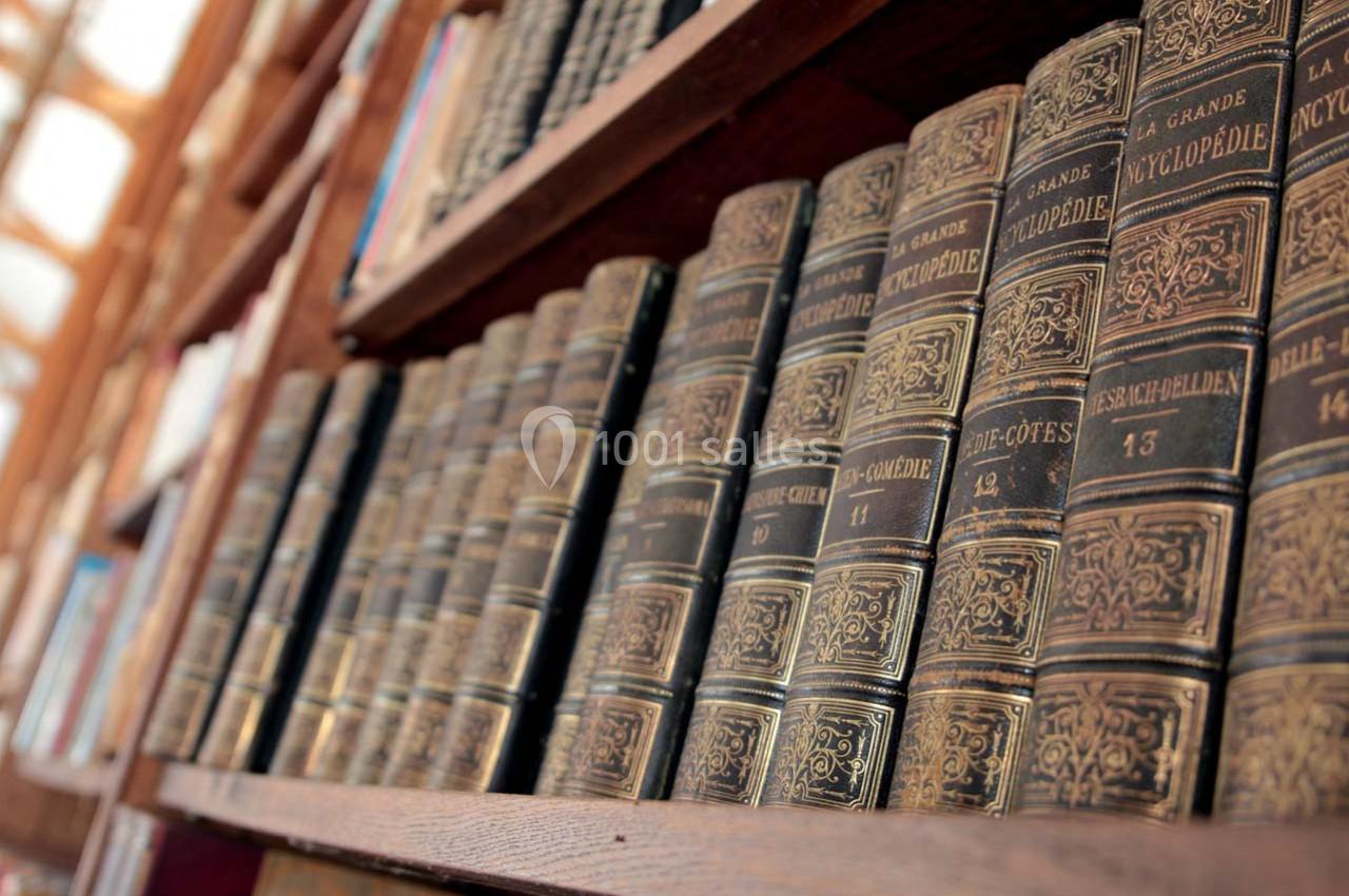 Rayonnage en bois contenant une collection de livres anciens aux reliures sombres et ornées de dorures.