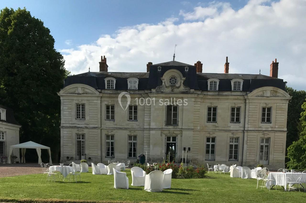 Façade d'un château ancien entouré de verdure, avec des tables et chaises blanches installées sur la pelouse.