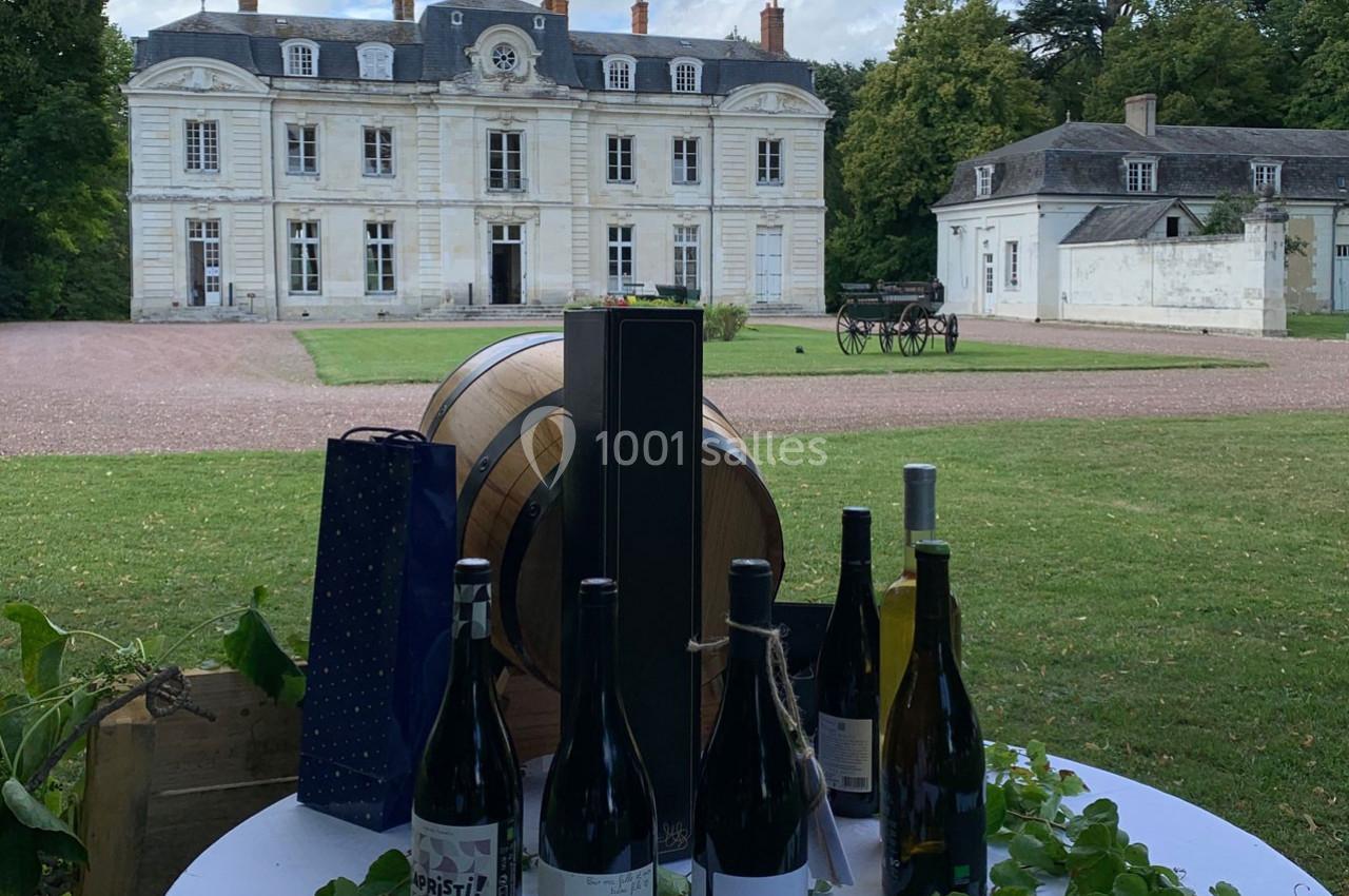 Bouteilles de vin et tonneaux exposés sur une table devant un château entouré de verdure.