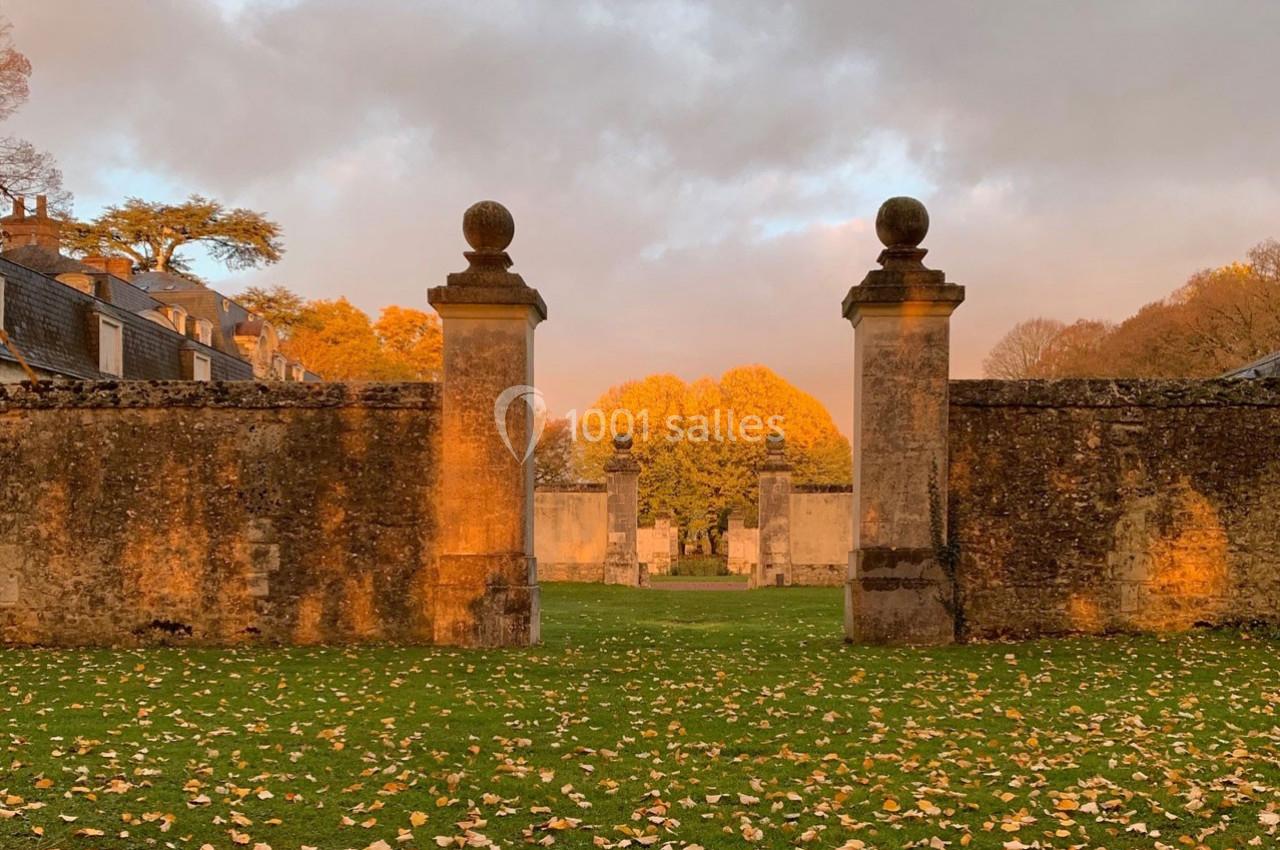 Portail en pierre encadrant une vue sur un parc arboré aux couleurs automnales, éclairé par une lumière dorée.