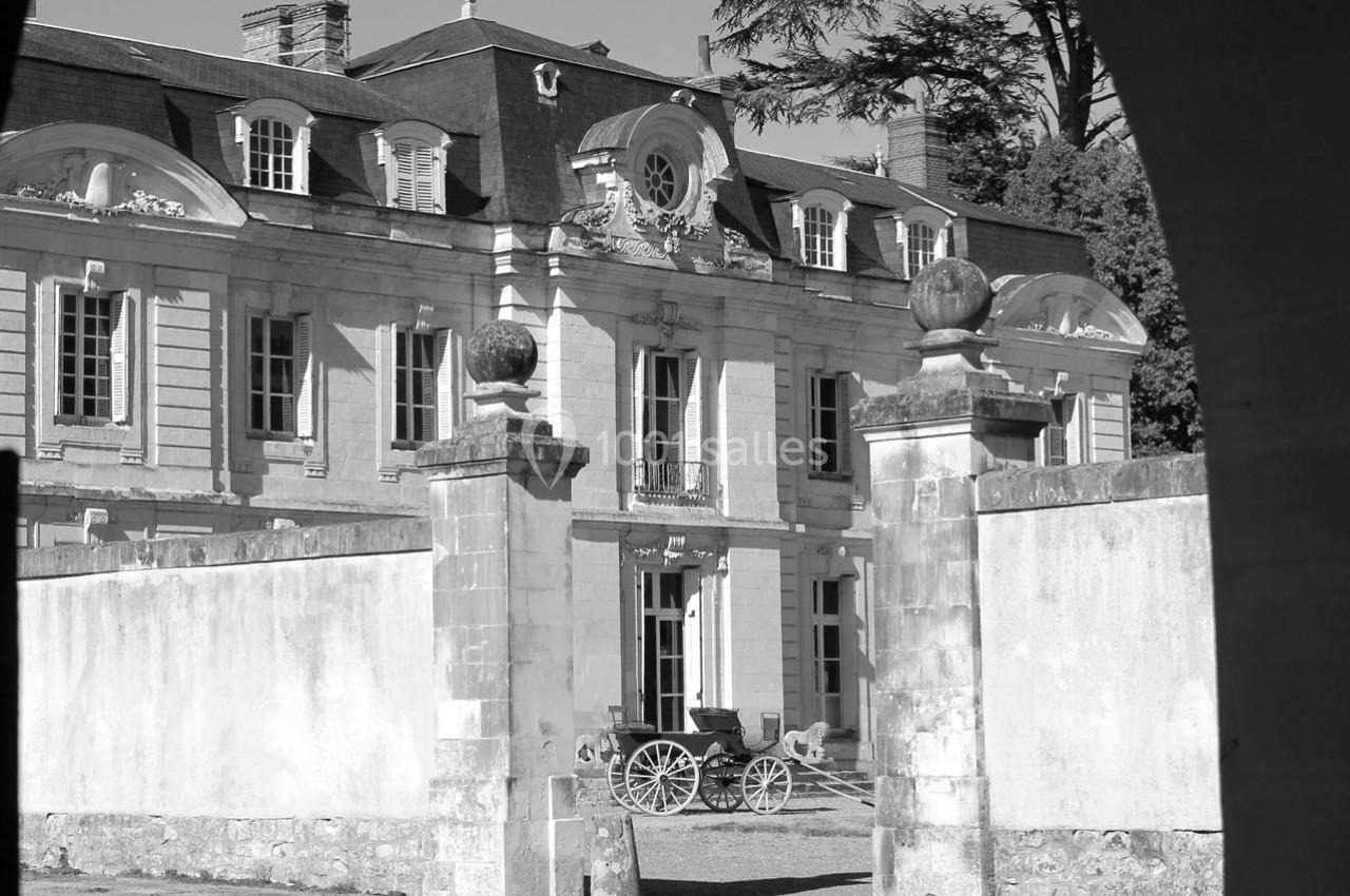 Façade d'un château ancien avec une calèche stationnée dans la cour, vue à travers une arche en pierre.