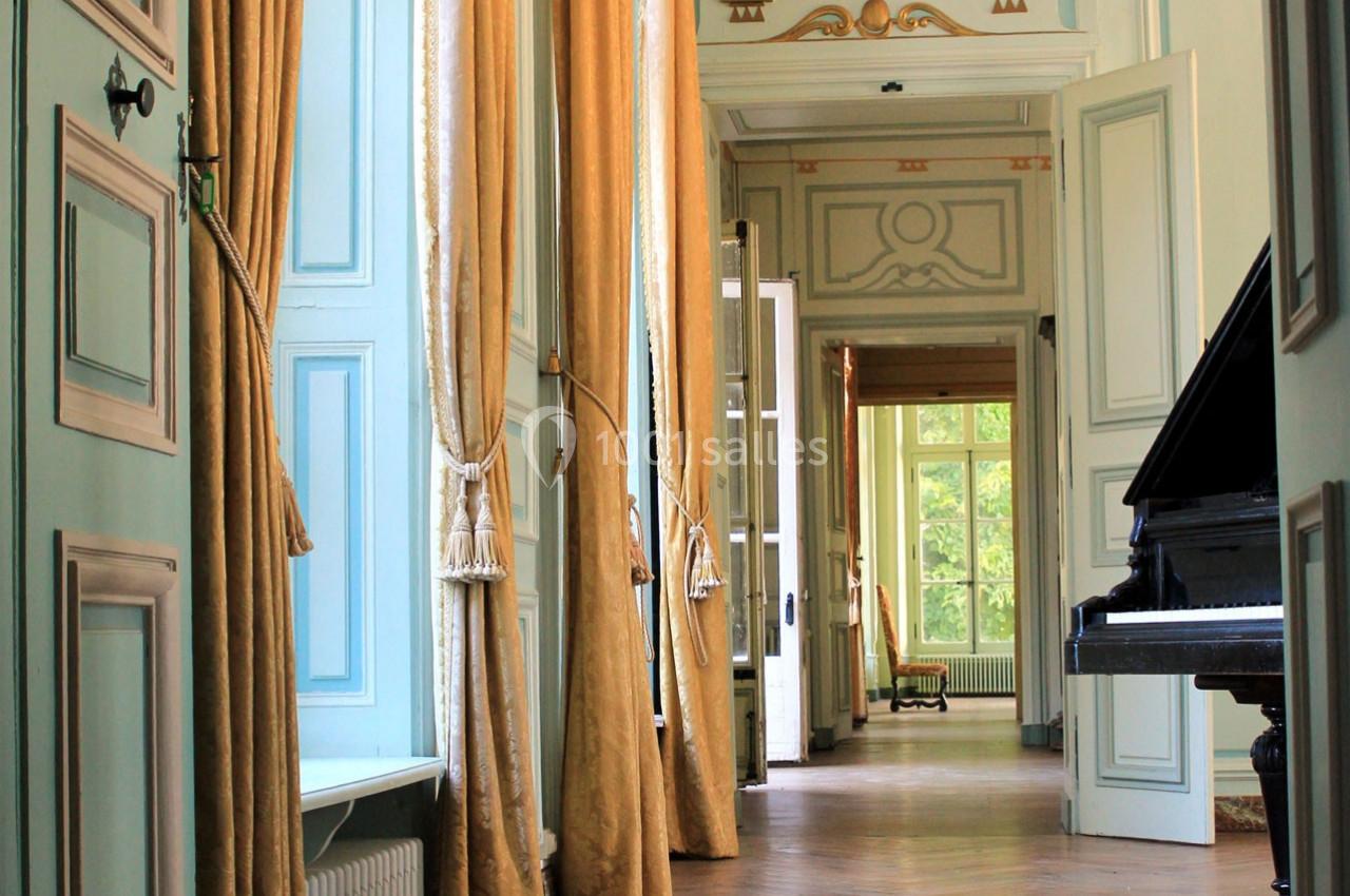 Intérieur lumineux avec des rideaux dorés, un piano noir et des portes ouvertes donnant sur un couloir élégant.